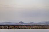 View of a distant group of people standing on a path surrounded by water and mountains under a pale sky, Magadi, Kajiado, Kenya.