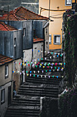 Porto, Portugal - 17. Juni 2022: Blick auf eine steile, schmale, mit bunten Wimpeln geschmückte Treppe, die sich durch alte Gebäude mit verwitterten Fassaden und Terrakotta-Dächern windet.