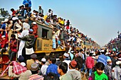 Dhaka, Bangladesh - 20 January 2018: View of a train packed with people, some perched precariously on top, under a bright sky, creating a scene of vibrant chaos and movement..