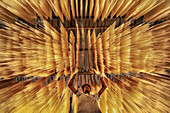 Bogura, Bangladesh - 23 March 2023: View of a worker amidst a golden canopy of drying noodles, creating a mesmerizing, textural landscape of light and shadow.