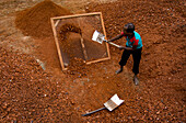 Gokul, Bangladesh - 11 June 2016: View of a worker sifting through heaps of reddish-brown earth with a sieve, the shovels glinting under the sun, creating a scene of labor against the textured ground.