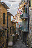 View of the narrow street with old buildings and flags waving gently in the breeze, a timeless slice of Italian life, Passignano sul Trasimeno, Umbria, Italy.
