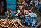 Kolkata, India - 28 January 2023: View of three elderly men in a Kolkata market, one gesturing animatedly while another thoughtfully smokes, amidst piles of produce.