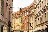 Blick auf farbenfrohe Gebäude in einer engen Straße, deren Fassaden in Pfirsich-, Gelb- und Orangetönen gestrichen sind, mit einem Netz von Drähten darüber, Graz, Österreich.
