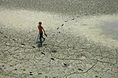 Mirsharai, Bangladesch - 17. August 2018: Ein einsames Kind durchquert die ausgedörrte Erde, seine Fußspuren ziehen sich durch die rissige Landschaft, wo einst Wasser floss, unter der harten Sonne.