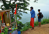 Sitakund, Bangladesh - 04 March 2019: View of two young men pause near a small stall, gazing out at the expansive, verdant hills under a soft, overcast sky.