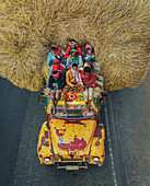 Bogura, Bangladesh - 08 February 2025: View of a vibrant yellow vehicle, packed with people and topped with a towering stack of golden hay, traverses the road.