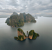 Aerial view of the iconic karst formations rise majestically from the emerald waters, creating a stunning contrast against the cloudy sky, Phang Nga Bay, Thailand.
