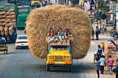 Bogura, Bangladesh - 03 January 2018: View of a yellow truck overloaded with hay and people, creating a striking contrast against the bustling street scene.