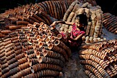 Bogura, Bangladesh - 20 May 2017: View of a young girl amidst a sea of earthen pottery, her red dress a vibrant contrast to the terracotta hues of the crafted vessels.