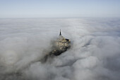 Luftaufnahme des Mont Saint-Michel, der durch ein Meer von ätherischem Nebel hindurchragt, seine alten Steine sind ein Leuchtfeuer der Geschichte in der nebligen Weite, Mont Saint-Michel, Normandie, Frankreich.