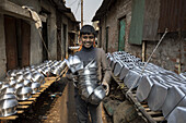 Keraniganj, Bangladesh - 27 December 2020: View of a young boy beaming with pride amidst rows of gleaming metal pots drying under the muted sunlight of a narrow street..