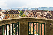 View of terracotta rooftops cascading across the historic skyline, framed by weathered stone and green bars, embracing the city's ancient beauty, Graz, Styria, Austria.