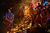 Bogura, Bangladesh - 20 November 2023: View of women in colorful saris gathered by the riverbank, offering glowing candles and flowers in a vibrant display of devotion.