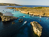 Aerial view of azure waters embracing rugged cliffs, boats dotting the serene bay under a clear sky, a vibrant dance of nature and leisure, Gozo, Gajnsielem, Malta.