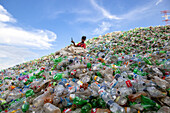 Chittagong, Bangladesh - 22 September 2022: View of a man amidst a colossal, colorful mountain of discarded plastic bottles under a vibrant blue sky.