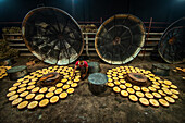 Bogura, Bangladesh - 05 February 2022: View of a worker amidst a sea of golden discs, contrasted by the dark, looming metal structures in the dimly lit space.
