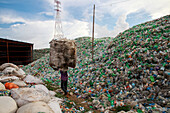 Chittagong, Bangladesh - 22 September 2022: View of a lone figure dwarfed by towering mountains of discarded plastic bottles under a vast, cloudy sky.
