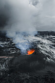 Luftaufnahme eines Vulkanausbruchs mit leuchtend orangefarbener Lava vor einer kahlen, monochromen Landschaft unter einem schweren, bewölkten Himmel, Grindavik, Region Südliche Halbinsel, Island.