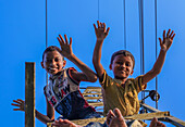 Mirsarai, Bangladesh - 06 August 2019: View of two joyful boys atop a structure, their arms raised against the clear sky, a playful moment captured from below.