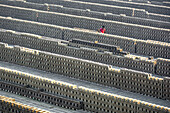 Gokul, Bangladesch - 12. Juli 2017: Blick auf eine einsame Figur in Rot inmitten der endlosen, rhythmischen Reihen von gestapelten Ziegeln, die einen starken Kontrast zu der gedämpften grauen Landschaft bilden.