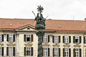 View of the baroque Holy Trinity column, a spiral of dark metal reaching skyward, against a backdrop of a building with many windows, Graz, Styria, Austria.