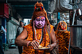Kolkata, India - 28 January 2023: View of a man with painted face, dressed in traditional attire and a distinctive hat, holds a plate of food amidst the bustling street.