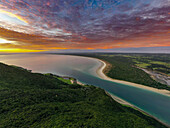 Luftaufnahme der ruhigen Flussmündung, die in den weiten Ozean mündet, unter einem leuchtenden Sonnenuntergangshimmel, der goldene und violette Farbtöne über die Landschaft wirft, Whangarei, Region Northland, Neuseeland.
