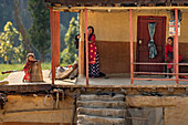 Dhangadhi, Nepal - 03 March 2023: View of a traditional mud house bathed in warm light, where women in vibrant saris smile from the porch, creating a scene of everyday life.