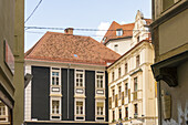 View of aged buildings with terracotta roofs and symmetrical windows exude historical charm under a soft sky, creating a timeless street scene, Graz, Austria.