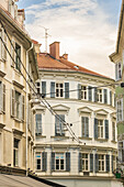 View of buildings with shuttered windows and an orange roof under a cloudy sky, revealing European architecture, , Graz, Austria.