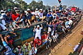 Dhaka, Bangladesh - 20 January 2018: View of a train, crammed with people, some waving the Bangladesh flag, a vibrant display of unity amidst the urban landscape.