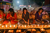 Narayanganj, Bangladesh - 11 June 2018: View of women in vibrant sarees kneeling amidst the warm glow of numerous earthen lamps, their light dancing on serene faces.