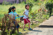 Dhangadhi, Nepal - 03 March 2023: View of two joyful girls with faces smeared with vibrant colors, playfully wielding water guns amidst the lush greenery.