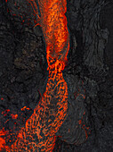 Luftaufnahme von geschmolzener Lava, die wie ein feuriger Fluss durch die dunkle, zerklüftete Landschaft fließt, ein starker Kontrast aus leuchtendem Orange und tiefem Schwarz, Grindavik, Region Südliche Halbinsel, Island.