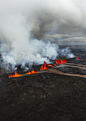 Luftaufnahme eines feurigen Vulkanausbruchs, der die Landschaft mit Flüssen aus geschmolzener Lava vor dem Hintergrund eines dunklen, bedrohlichen Himmels überzieht, Grindavik, Region Südliche Halbinsel, Island.