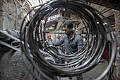 Keraniganj, Bangladesch - 27. Dezember 2020: Blick auf einen Arbeiter, der in einer schwach beleuchteten Werkstatt konzentriert seiner Arbeit nachgeht, eingerahmt von Metallspulen, die Szene ist erfüllt von den düsteren Strukturen der Industrie.