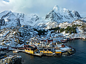 Aerial view of vibrant yellow buildings nestle against the stark white of snow-capped mountains in the Lofoten Islands, a stunning contrast of color and texture., Norway.