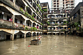 Chattogram, Bangladesch - 05. August 2023: Blick auf die Überschwemmungen in den Innenhöfen von Gebäuden, in denen sich der Himmel spiegelt, während ein Kind auf einer Betonstruktur inmitten von Treibgut steht.
