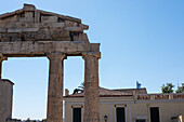 View of weathered stone columns stand in stark contrast against the clear blue sky, framing a glimpse of a building with a Greek flag, Athens, Central Athens Regional Unit, Greece.