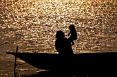 Bogura, Bangladesh - 06 February 2017: View of a silhouetted mother and child in a small boat, against a backdrop of shimmering golden water, evokes a sense of serene beauty.
