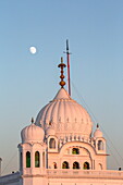 View of the pristine white dome of Gurdwara Darbar Sahib gleams under the soft glow of the moon, a beacon of faith in Kartarpur, Punjab, Pakistan.