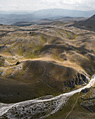 Die Luftaufnahme der sonnenverwöhnten, zerklüfteten Landschaft entfaltet sich unter einem dunstigen Himmel und enthüllt die einzigartige Schönheit von Campo Imperatore, Gran Sasso, Abruzzen, Italien.
