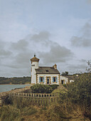 View of the quaint The Phare de Nantouar with blue shutters stands proudly against the backdrop of the sea and sky, a peaceful scene, Louannec, Bretagne, France.