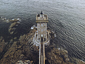 Aerial view of Phare de Kermorvan, a stone sentinel standing proud against the surging sea, connected by a narrow causeway, Le Conquet, Bretagne, France.