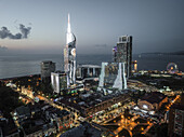 Luftaufnahme von beleuchteten Wolkenkratzern und dem Alphabet Tower in der Nähe des Riesenrads, einer modernen Stadtlandschaft, die sich von der Küste aus erhebt, Batumi, Adscharien, Georgien.