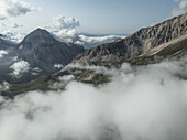 Luftaufnahme von majestätischen Bergen, die ein Wolkenmeer durchbrechen und felsige Gipfel und grüne Hänge in Campo Imperatore, Gran Sasso, Abruzzen, Italien, zeigen.