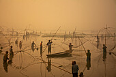 Pabna, Bangladesh - 28 November 2023: View of the Ruhul Bill's misty expanse, where silhouettes of men with towering fishing gear pierce the tranquil waters.