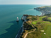 Luftaufnahme der dramatischen weißen Klippen, die auf das türkisfarbene Meer treffen, im Kontrast zu dem üppig grünen Golfplatz und der charmanten Stadt an der Küste, Étretat, Normandie, Frankreich.