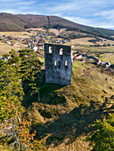 Aerial view of the stark stone ruins of the medieval Víglaš Castle tower rising above a grassy hill under a clear blue sky, Podzámcok, Banská Bystrica Region, Slovakia.